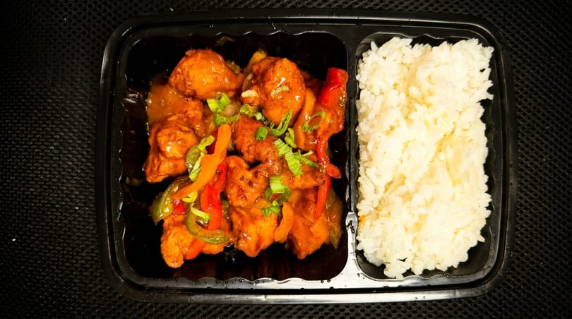 Takeout container with orange chicken, bell peppers, green onions, and white rice.